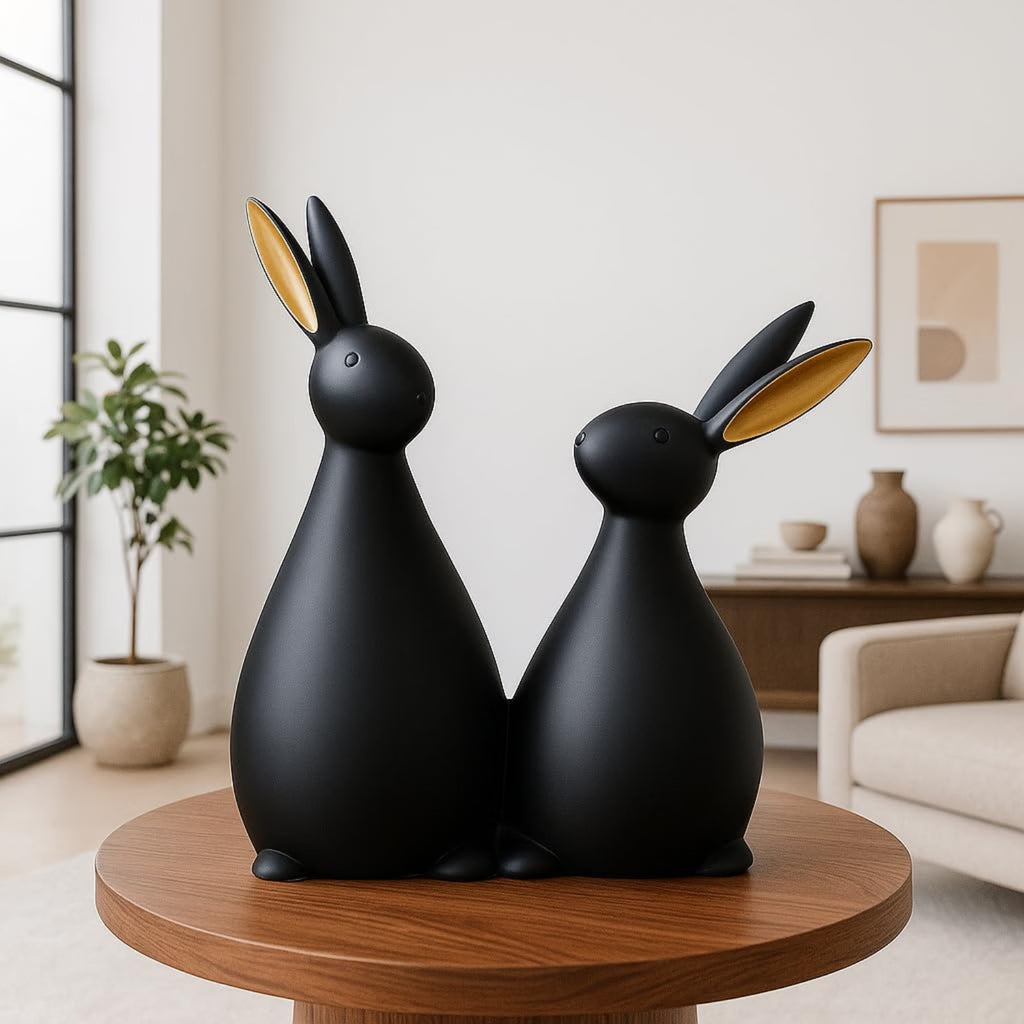 Two matte black rabbit-shaped decorative sculptures with gold-toned inner ears, displayed side by side on a round wooden table in a modern living room setting.