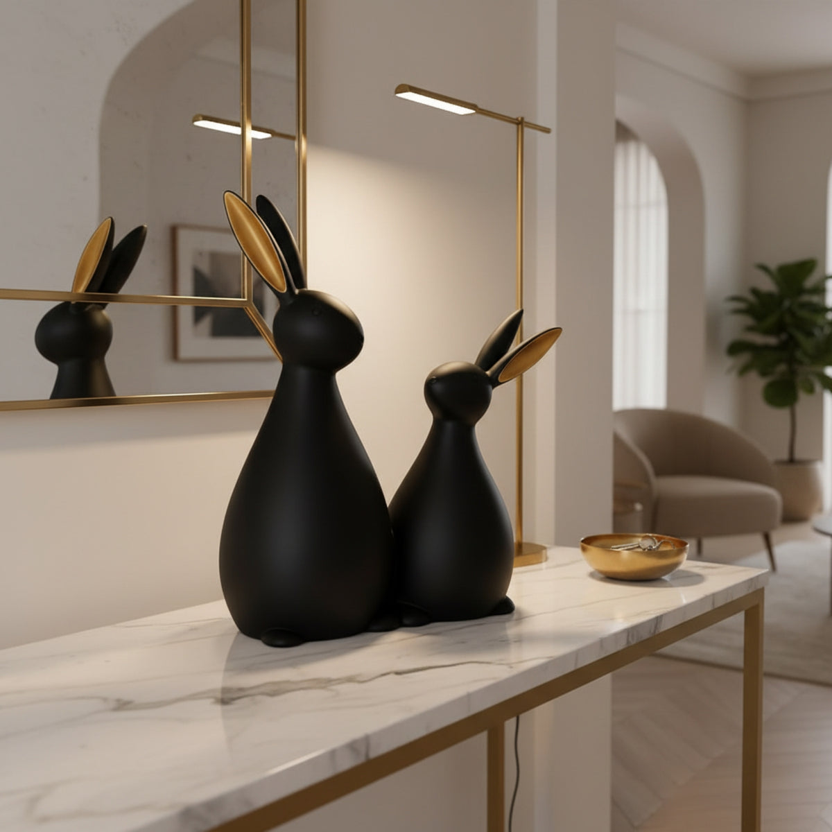 Two matte black rabbit-shaped decorative sculptures with gold-toned inner ears sit on a white marble console table in a modern interior with gold accents, a mirror, and a floor lamp.
