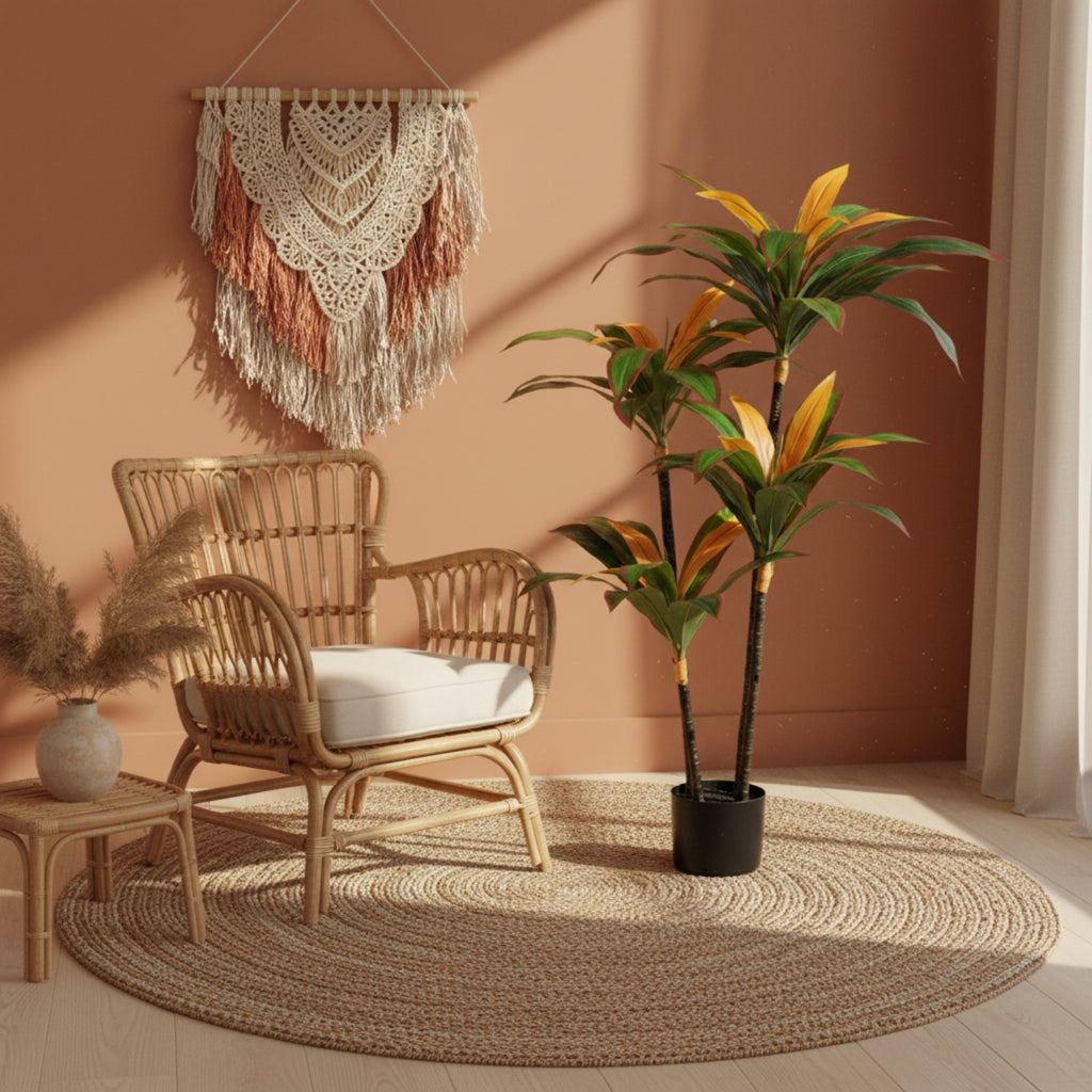 A styled boho room scene featuring a natural rattan armchair with a white cushion, a large round braided jute rug, a potted tropical plant, and a cream macrame wall hanging against a terracotta-colored wall.