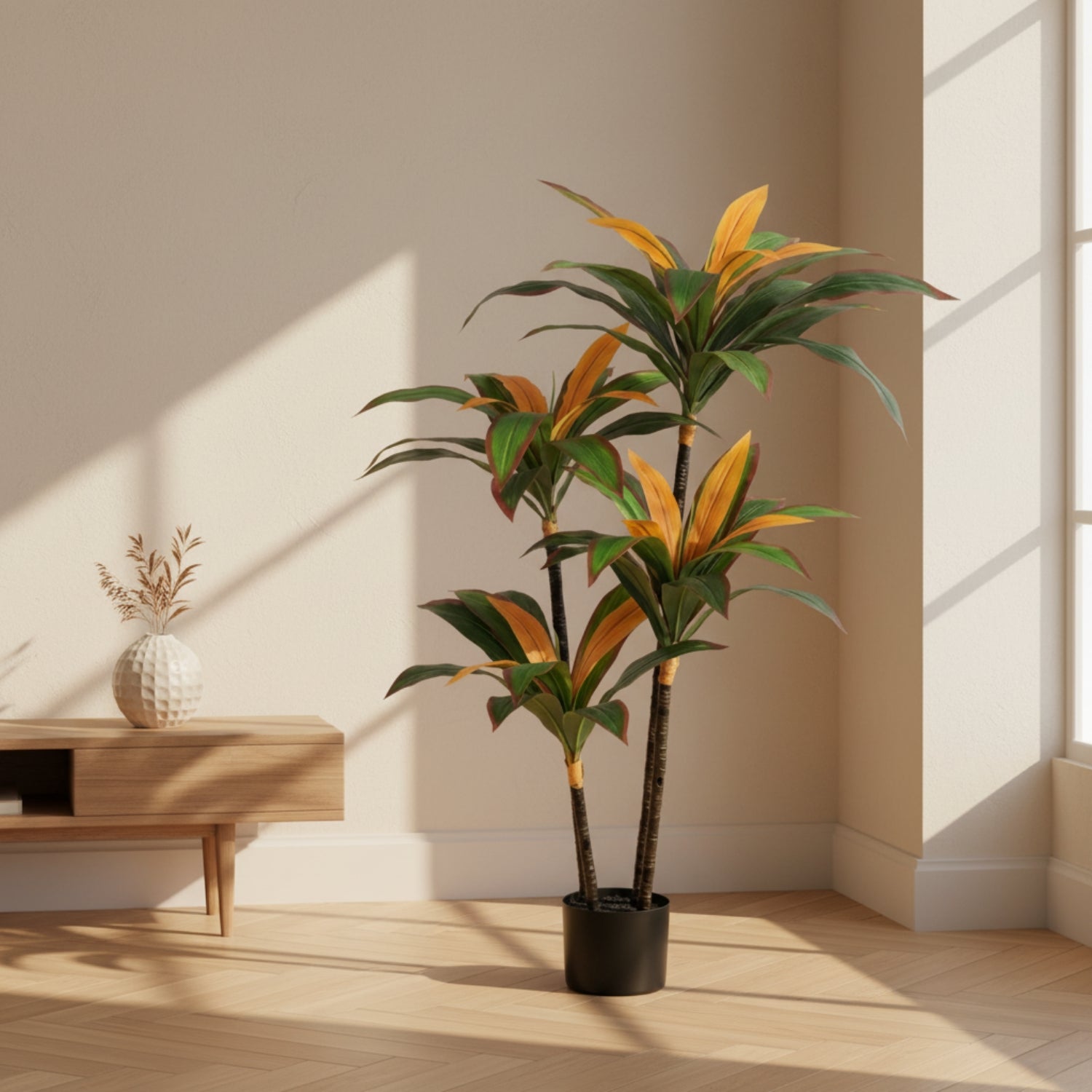 An artificial Dracaena massangeana houseplant with green and orange variegated leaves in a black pot, placed in a minimalist room with beige walls, light wood flooring, and a small wooden side table.