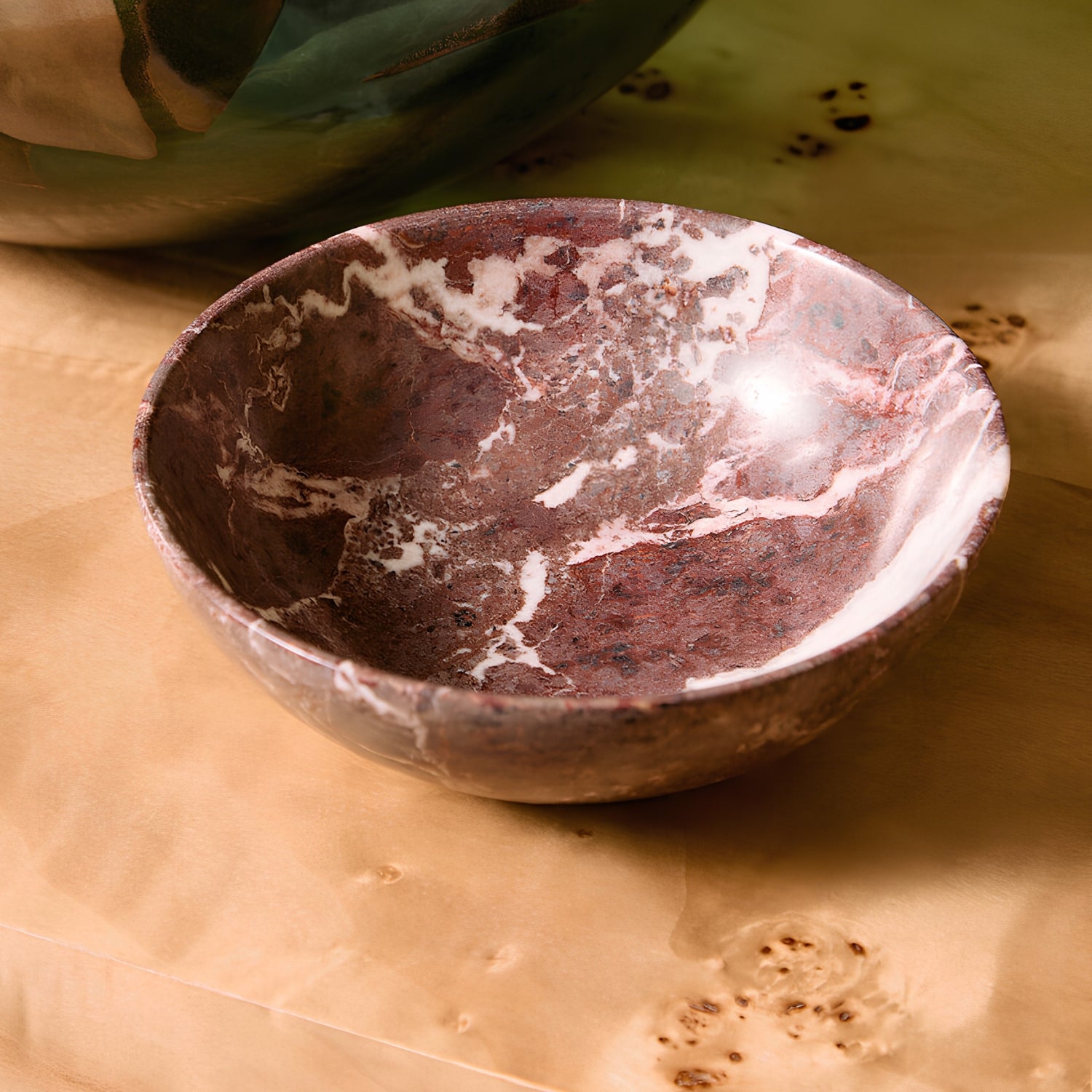 A handmade stone bowl with a reddish-brown and white marbled pattern, resting on a textured brown paper background.
