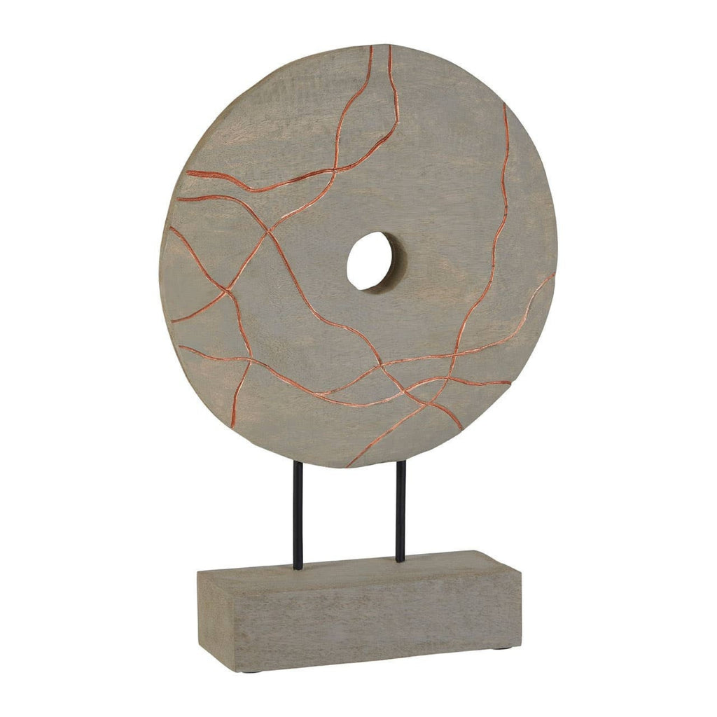 A decorative stone-like circular sculpture with a central hole, mounted on a rectangular base with two thin black legs. The top disc is light gray with thin copper-orange veining, set against a plain white background.