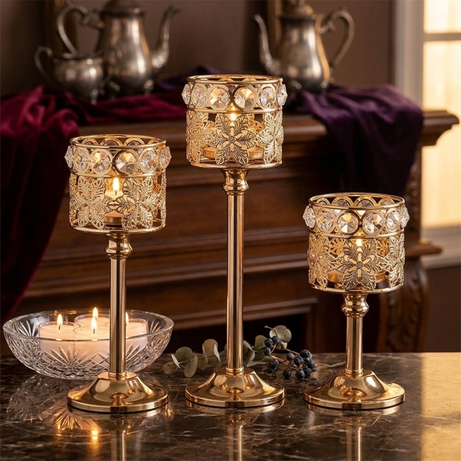Three ornate gold candlestick holders with crystal accents are arranged on a dark marble table, with lit candles in a glass bowl and a warm, elegant interior background.
