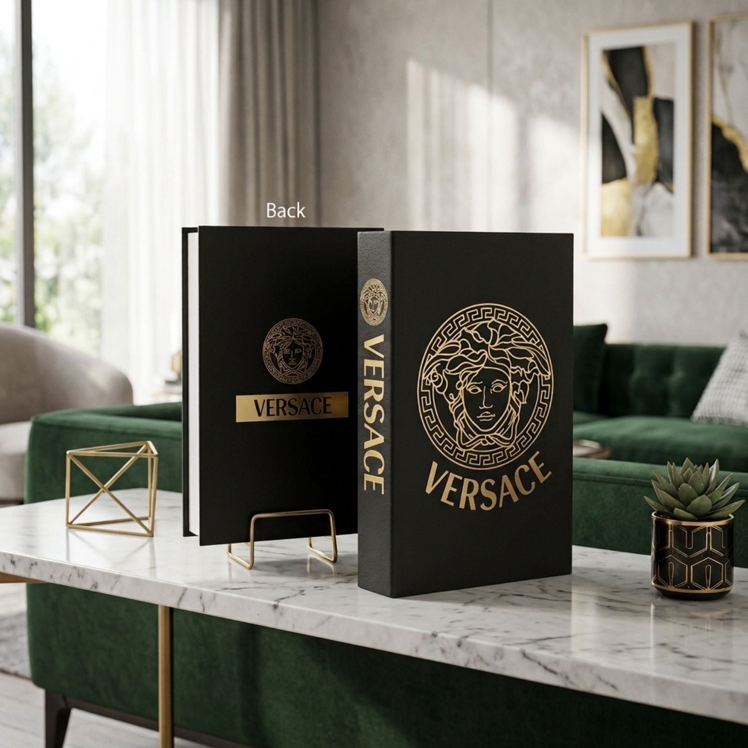 A black Versace hardcover book or notebook standing upright on a marble-topped table in a modern living room. The cover features a large gold circular Medusa emblem and the word VERSACE, with a smaller gold logo on the spine.