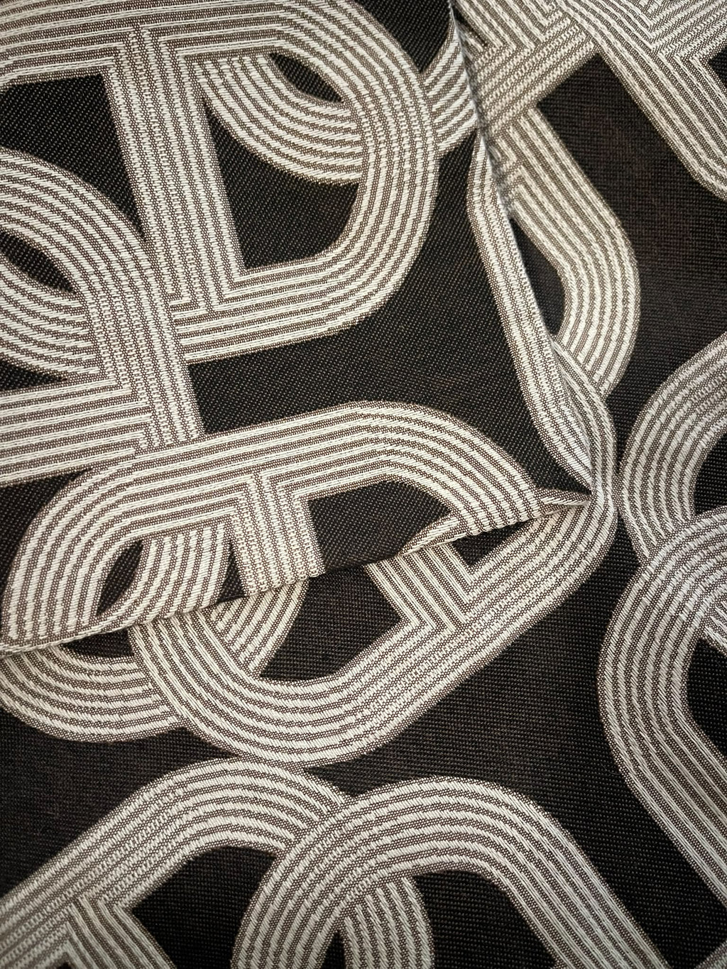 Close-up of the light-toned interlocking chain link pattern on dark cushion fabric
