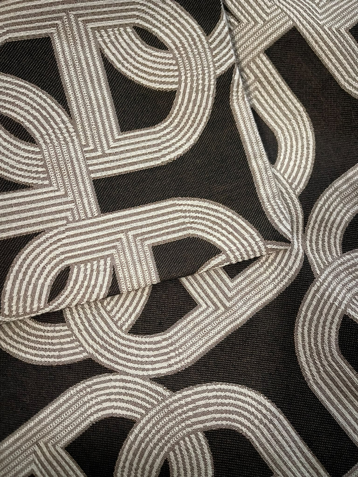 Close-up of the light-toned interlocking chain link pattern on dark cushion fabric
