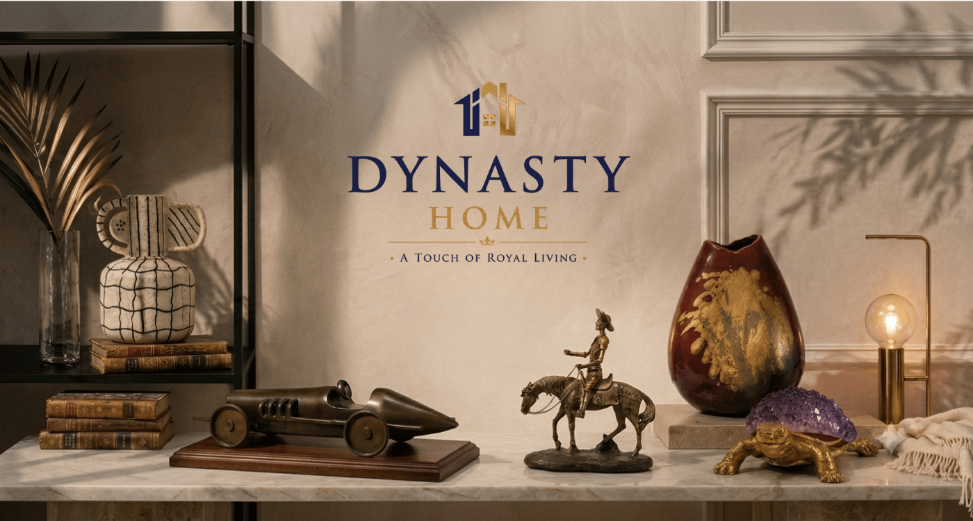 A styled interior scene with the words 'DYNASTY HOME' centered on a wall above a marble surface. The setting includes decorative objects such as a race car model, a horse-and-rider figurine, a patterned vase, a turtle figurine, a lamp, books, and shelving.