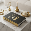 Gucci black and gold coffee table book styled on marble side table in modern luxury living room with cream sofa and natural light